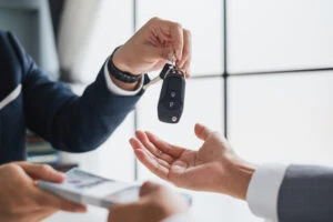 An agent from a rental car company hands the key to a customer. After a car accident,  insurance will pay for the rental car after an accident for as long as it is deemed reasonable. A car accident lawyer can explain your policy and work to ensure you receive fair rental car coverage after the crash.