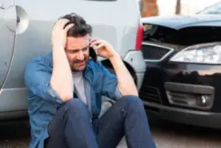 A man talks on his phone next to a car accident
