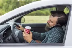 motorist holding cup and using phone while behind the wheel