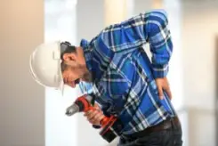 A construction workers holding a drill bent over with back pain