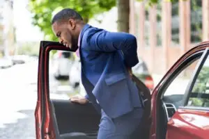 black man getting out of car with back pain