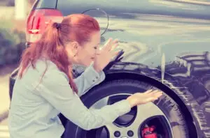 Mujer frustrada comprobando daños a su auto ¿Cuánto cuesta un abogado de accidentes de auto?