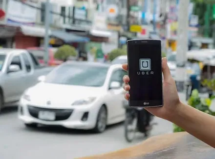 Person holding a smartphone with Uber on the screen and traffic blurred in the background.