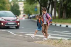 Girl and boy with backpacks carefully cross road on pedestrian crossing on their way to school.