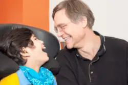 A child with cerebral palsy laughing with a caretaker