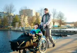 A parent pushing their child with erbs palsy in a wheelchair