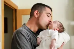 A parent kissing their newborn with erbs palsy on the side of the head