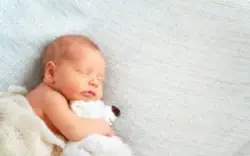 sleeping newborn clutching teddy bear