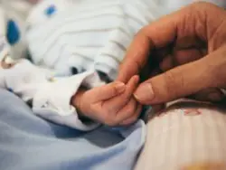 Baby with cerebral palsy is holding mom’s hand