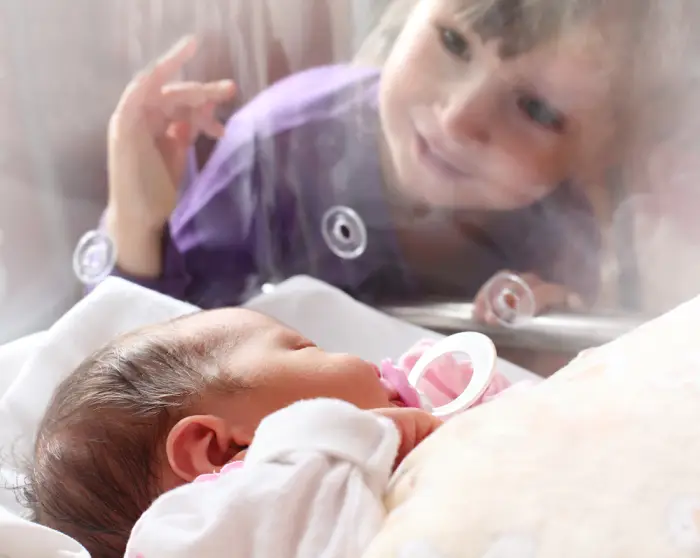 little girl visits baby sister sleeping in incubator