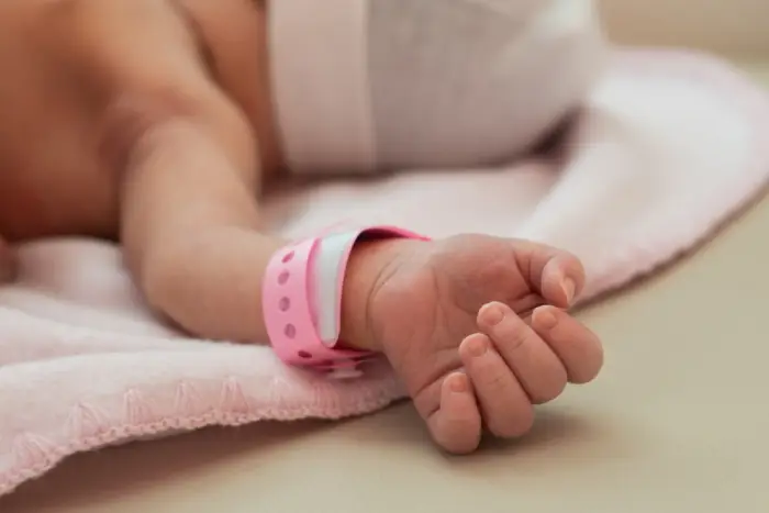 A newborn child lies on a blanket with a hospital bracelet around their wrist.