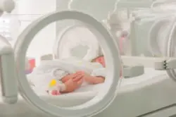 newborn baby hooked up to medical equipment in hospital bed