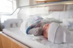 An infant sleeps in a hospital crib.