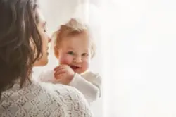 blushing baby looks over mother’s shoulder