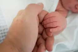 A baby with a birth injury holds a lawyer's finger. The attorney is investigating the cause of cerebral palsy.