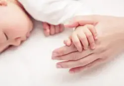 A birth injury lawyer holds a baby's hand. The legal professional investigates the medical mistake that caused cerebral palsy.