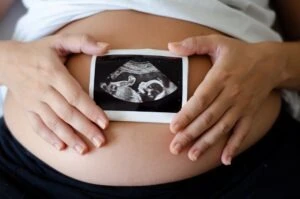 A pregnant woman holds an ultrasound image of the baby. She is experiencing symptoms that could be linked to intrauterine fetal demise. A birth injury lawyer can tell you more about intrauterine fetal demise.