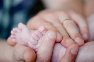 Mother holding baby’s feet. Can babies recover from lack of oxygen at birth?