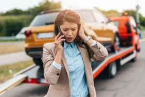 A woman on the phone in front of her car being towed. How long do truck accident cases take to settle in Texas?