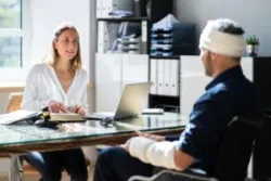 A man in a wheelchair with a bandaged head is talking to a personal injury lawyer about when he should file a traumatic brain injury claim.