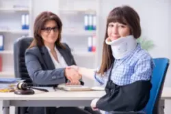 Woman in sling and neck brace shakes hands with product liability lawyer.