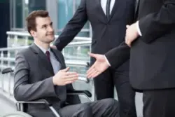 Two male lawyers greet a disabled man who is in a wheelchair.