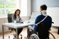 A severely injured man in a wheelchair wearing a neck brace and an arm sling while discussing his case with an experienced catastrophic injury lawyer in New Haven.