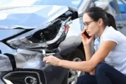A woman examining the damage to her vehicle while calling an experienced car accident lawyer in Hartford.