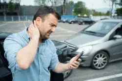 An injured man at the scene of a crash, rubbing his neck and calling a lawyer to protect his rights following a car accident.
