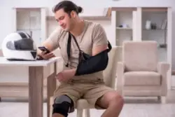 An injured motorcyclist with an arm sling and a knee brace, calling a lawyer to protect his rights following a motorcycle accident.