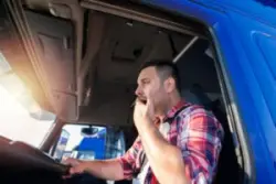 A fatigued truck driver is yawning while driving.