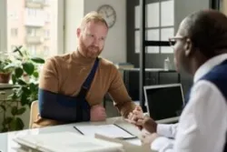 An injured man with his arm in a sling speaking with a workers’ compensation lawyer in Connecticut.