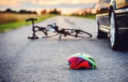 A bicycle and a helmet lie on the road next to a car. A Waterbury bicycle accident lawyer can help injured victims file a claim against the negligent driver.