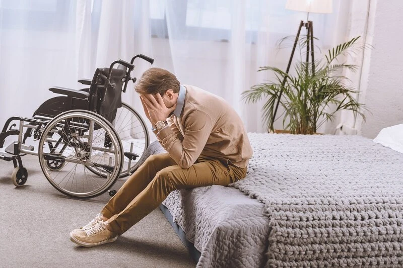 Disabled man sitting on bed holding head