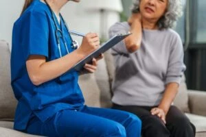 An elderly woman holds her neck while she asks her doctor: Is spondylosis a disability?