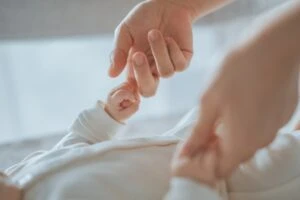 A mother holds her baby's hands. Long Term Disability may cover her maternity leave because she suffered severe complications during childbirth.