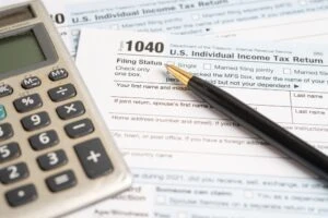 A calculator and pen rest on a Form 1040 while somebody off-camera wonders: Is Social Security Disability back pay taxable?