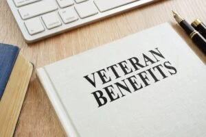 A book titled "Veterans Benefits" sits on a desk. Financial compensation, free healthcare, educational support, and housing assistance are among the benefits you can receive with a 100% VA disability rating. To apply or challenge a denied claim, consult with a VA disability lawyer.