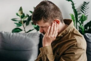 A man holds his ear as he reacts to discomfort from a tinnitus ear condition. The VA rating for tinnitus is 10%, whether it affects one ear or both ears. You can consult with a VA Disability lawyer if your claim for tinnitus is denied.