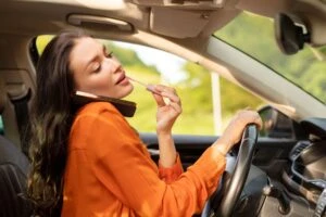 A woman dangerously distracted while driving, doing her makeup and talking on the phone.