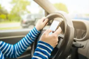 Woman driving car and texting message on smartphone, using mobile phone device while driving, dangerous and risky behavior in traffic