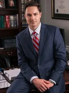 Attorney Evan L. Kaine sits on the edge of his desk in front of legal documents and books.