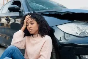 Woman upset sitting next to a damaged car.