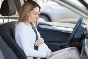 pregnant woman cradling her stomach in driver’s seat