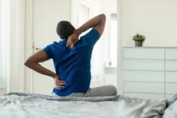 black man with back pain sitting on bed