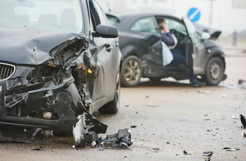 Two dark-colored cars with accident damage and a passenger making a phone call.