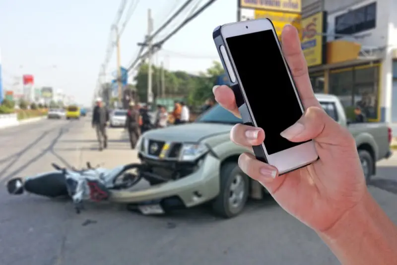 A motorist taking pictures with a cell phone after a motorcycle accident.