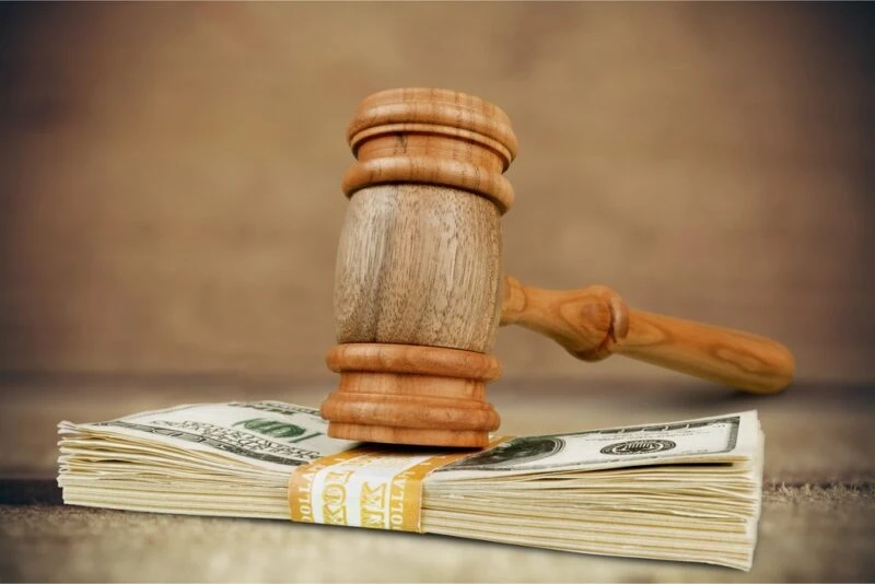 An image of a gavel resting on a stack of money representing a settlement. Wrongful death settlements pay out slightly differently than regular settlements because they can be split among many parties.