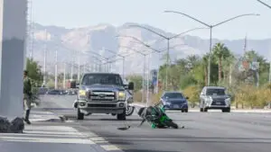 A motorcycle lying on its side on a busy highway with a pickup truck behind it and a backdrop of the Nevada mountains.
