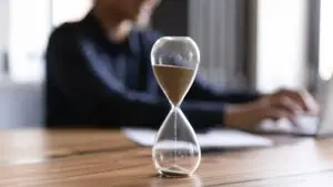 An hourglass and a man typing on the laptop in the background.
